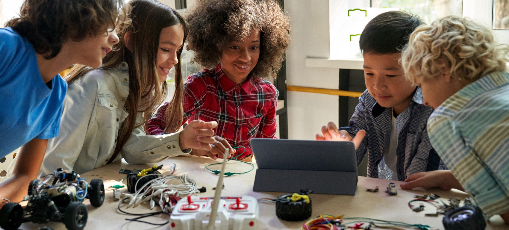 Stock image of diverse school children students group building robotic vehicle robot cars using tablet computer education software apps