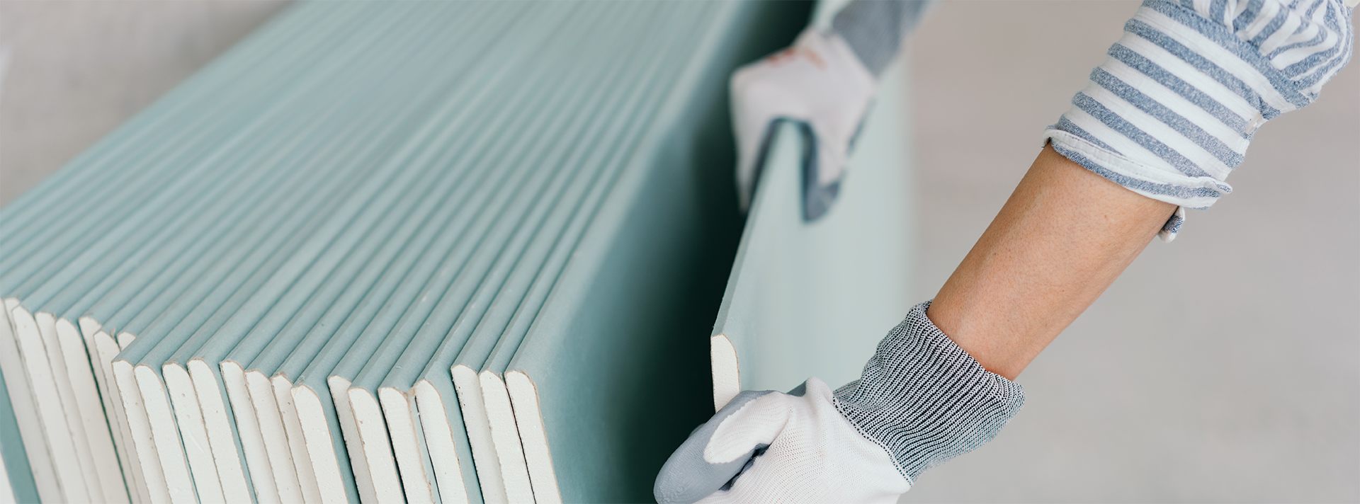 Sheets of drywall being leaned against a wall by a person wearing gloves